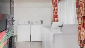 A compact kitchen with white appliances, a tiled floor, and a colorful wall decoration.
