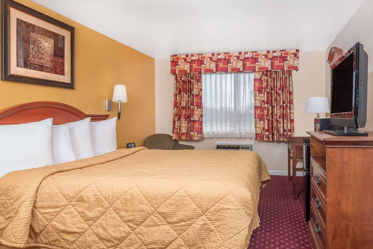 A hotel room with a large bed, a television, a desk, and a chair.
