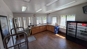 A kitchen with wooden cabinets, a refrigerator stocked with beverages, and a window with blinds.