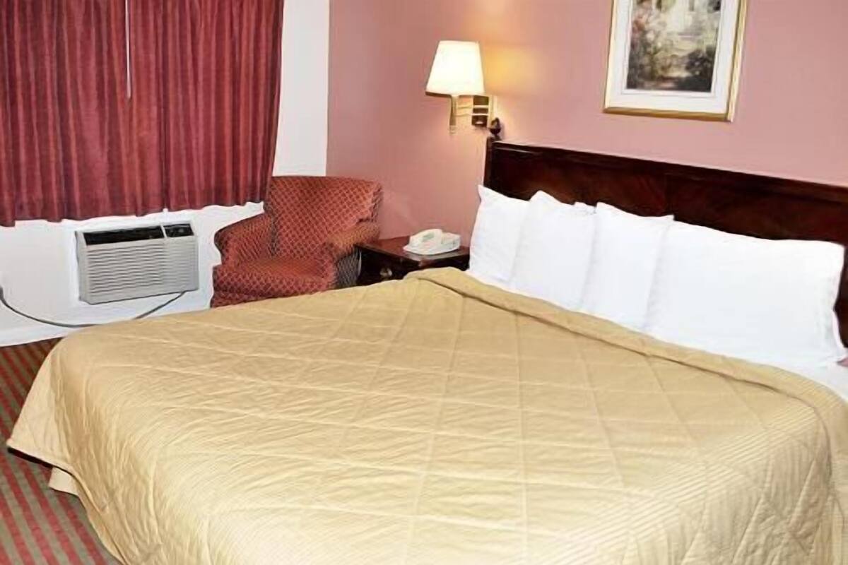 A hotel room with a large bed, a chair, a nightstand, a lamp, and a painting on the wall.