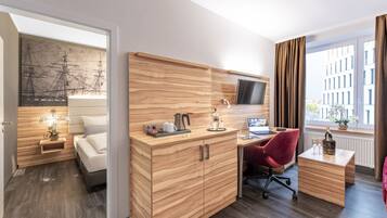Una habitación de hotel moderna con un escritorio de madera, una silla roja, un televisor montado en la pared y un amplio ventanal con cortinas.