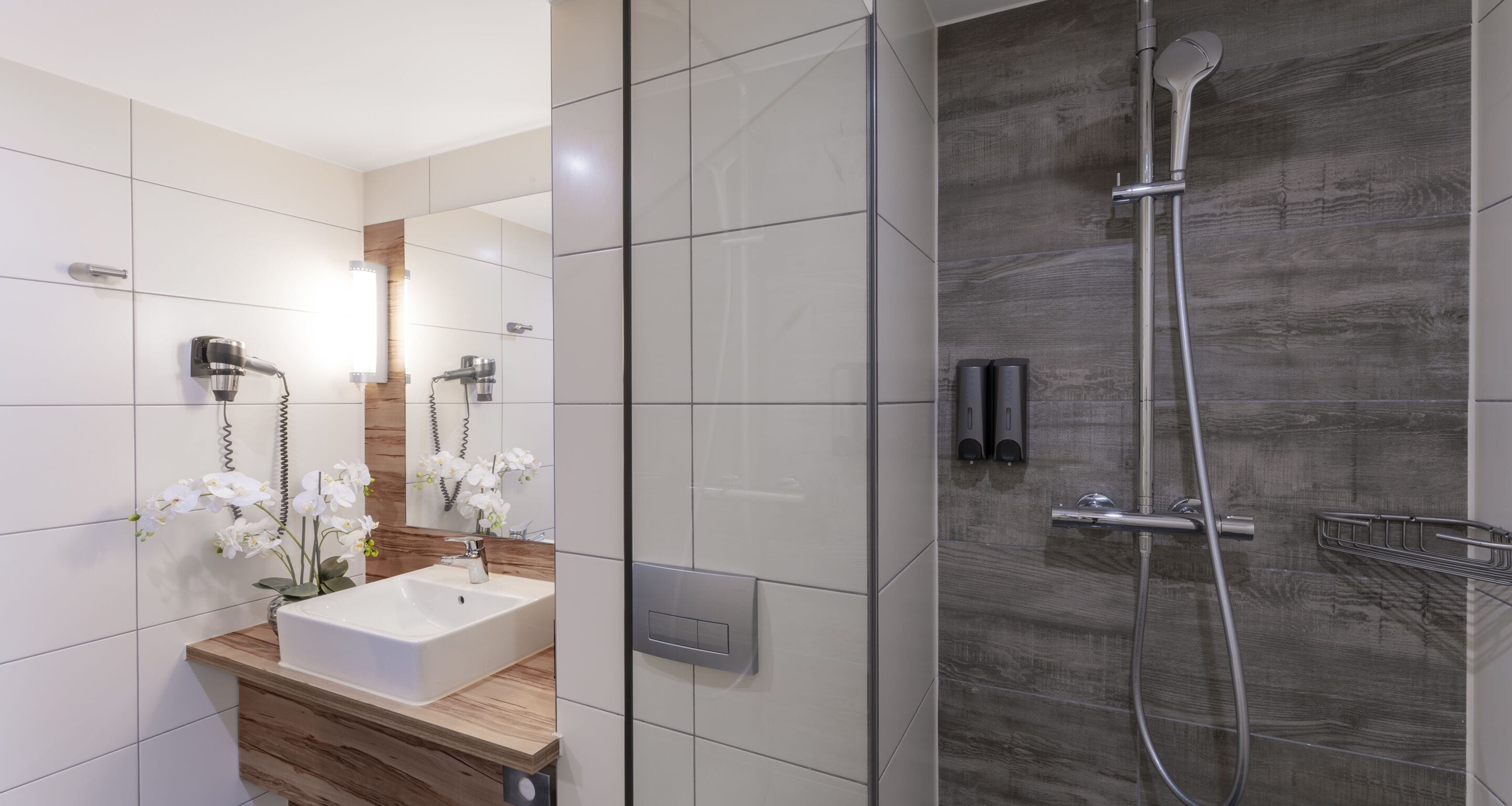 A modern bathroom with a large mirror, a sink, and a shower.
