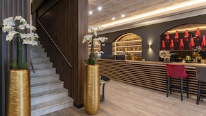 Un bar moderno con mostrador de madera, botellas rojas y una escalera con un jarrón dorado.