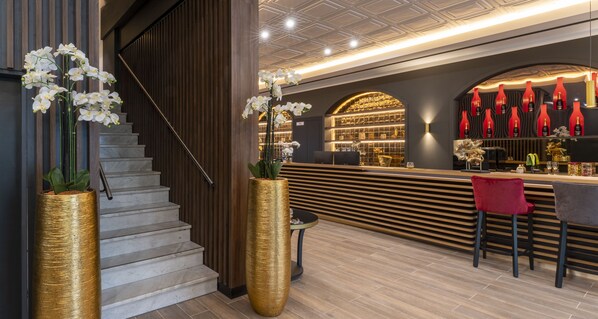 A modern bar area with a wooden counter, red bottles, and a staircase with a golden vase. - PLAZA Premium Columbus Bremen (Bremen)