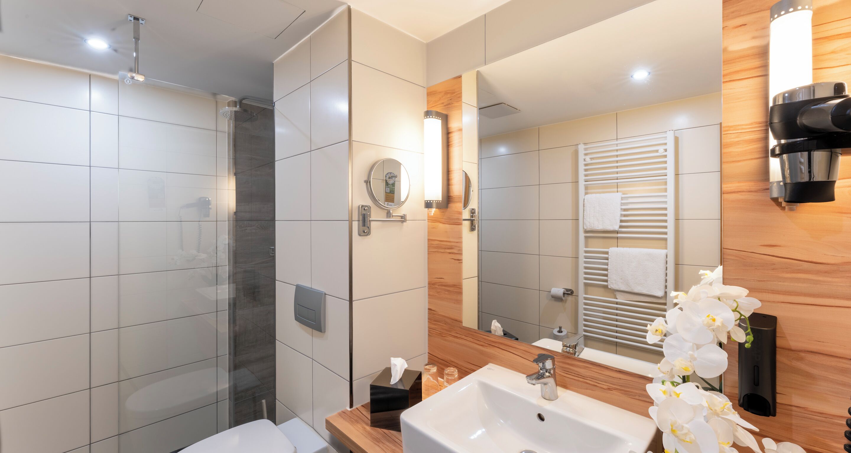 A modern bathroom with a glass shower enclosure, a sink, a mirror, and a towel rack.