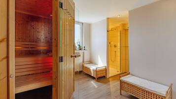 Una habitación moderna con sauna de madera, cabina de ducha de vidrio y una cama pequeña de madera.