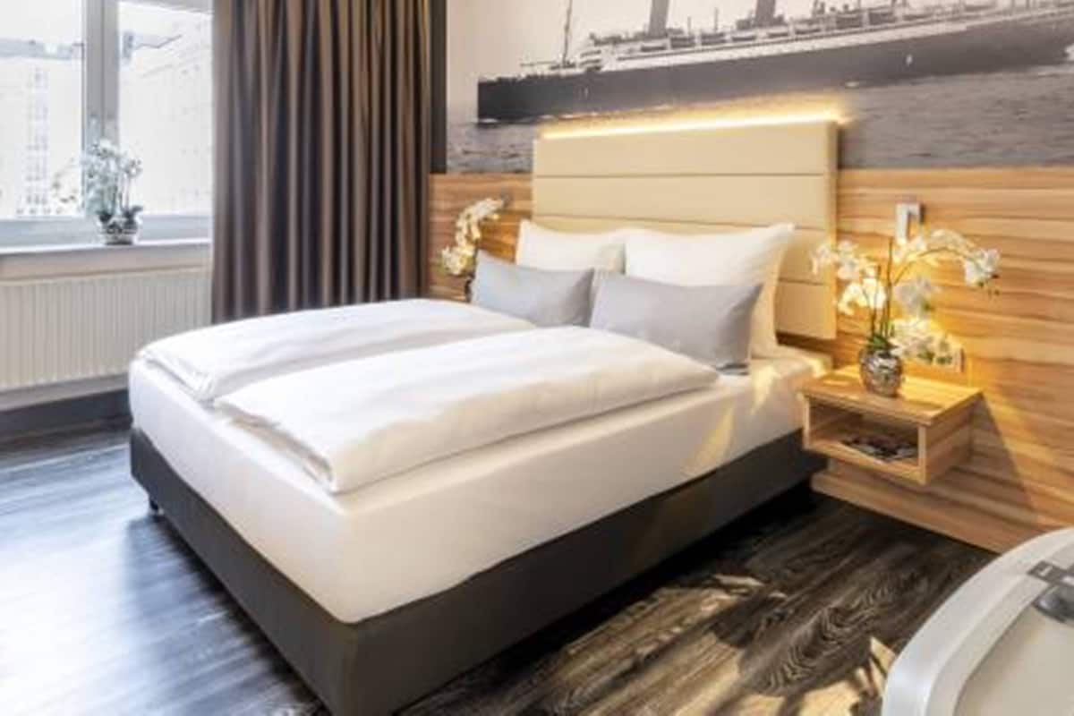 Camera d'albergo moderna con un grande letto, poggiatesta in legno, comodino con lampada e vista su una nave dalla finestra.