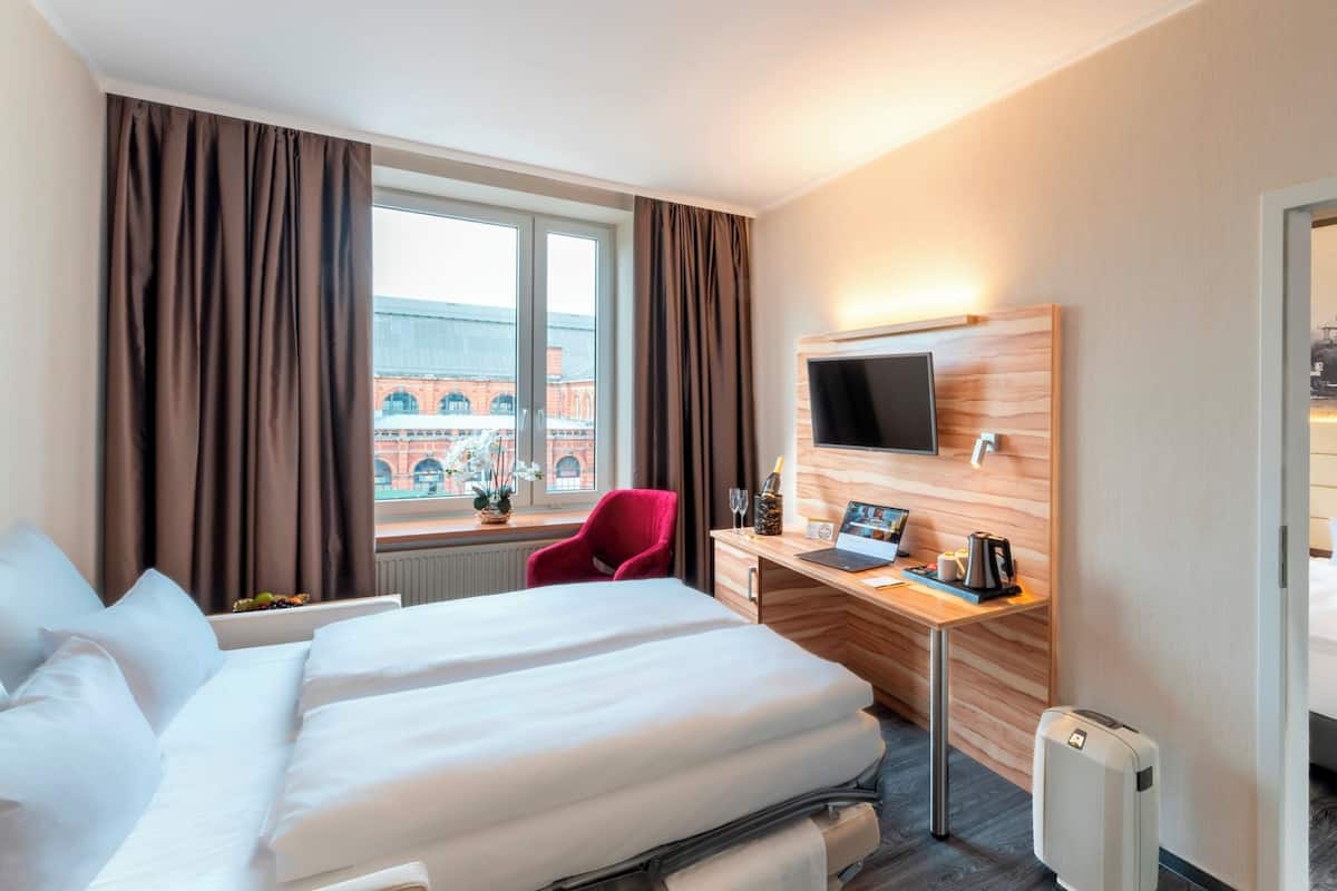 Una camera d'albergo con due letti, una scrivania con un portatile, una sedia rossa e una televisione.