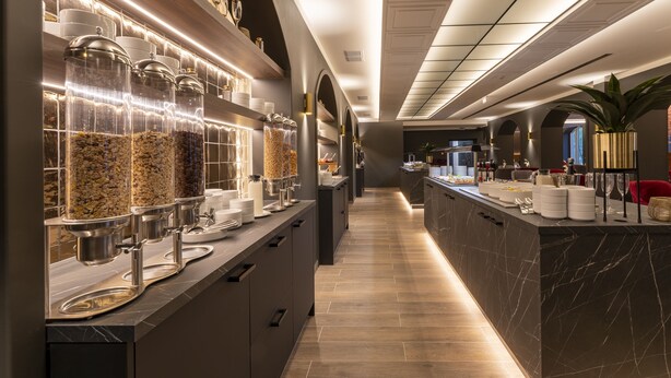 Un moderno vestíbulo de hotel con un mostrador de recepción de mármol, una exposición de alimentos con frascos de aperitivos y una planta en la esquina.