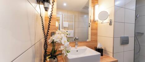 Un baño con lavamanos blanco, espejo y ducha.