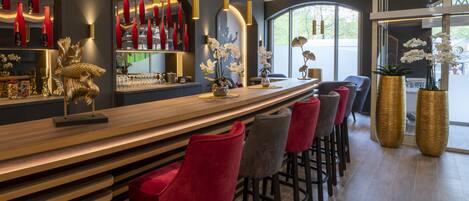 Un área de bar moderna con mostrador de madera, taburetes de bar rojos y grises, y detalles decorativos como una escultura de pez y orquídeas.