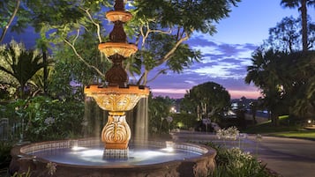 Ein mehrstufiger Brunnen mit herabfließendem Wasser, umgeben von üppigem Grün und Bäumen.
