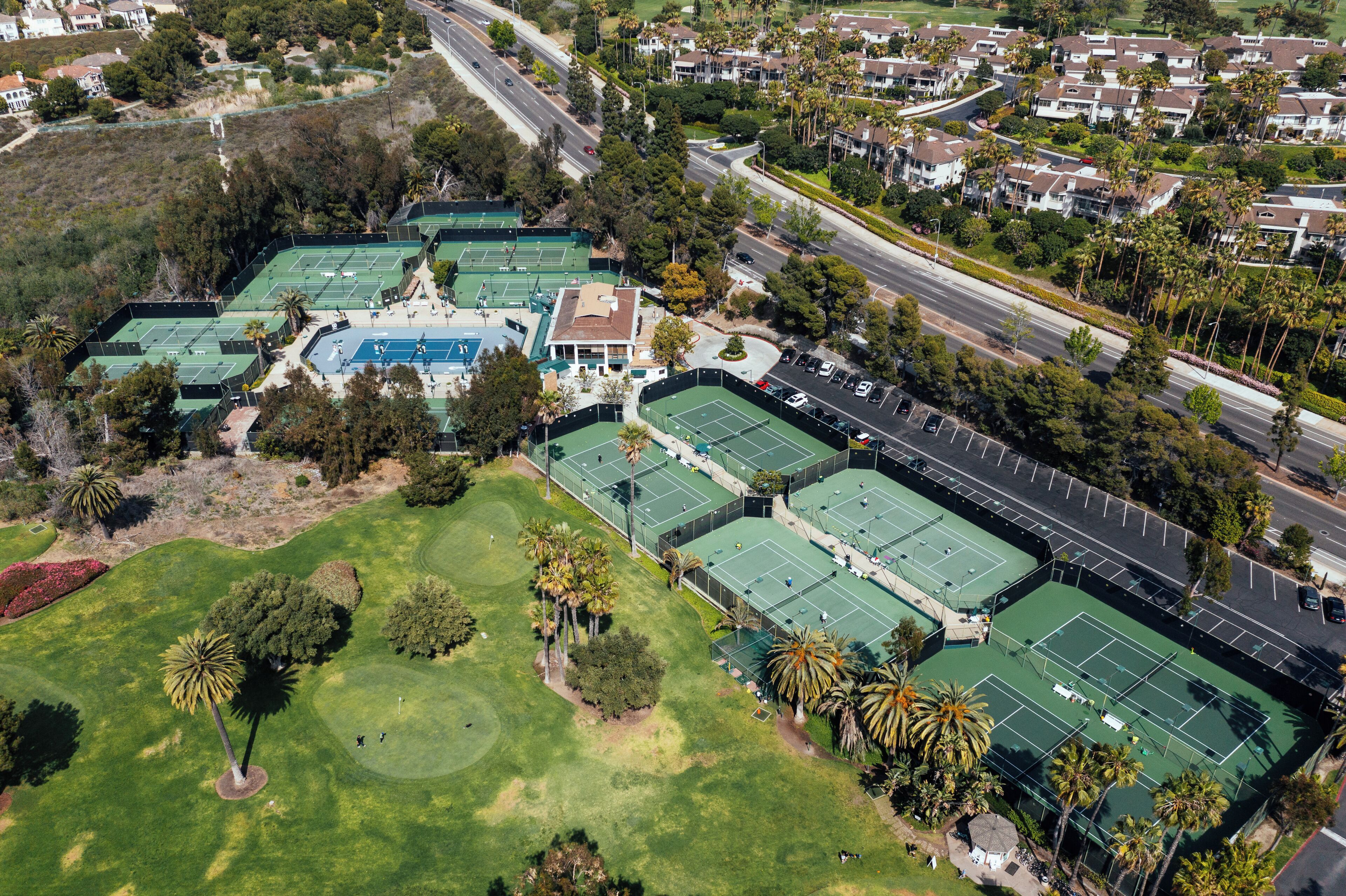 An aerial view of a residential area with multiple tennis courts, a golf course, and surrounding houses.