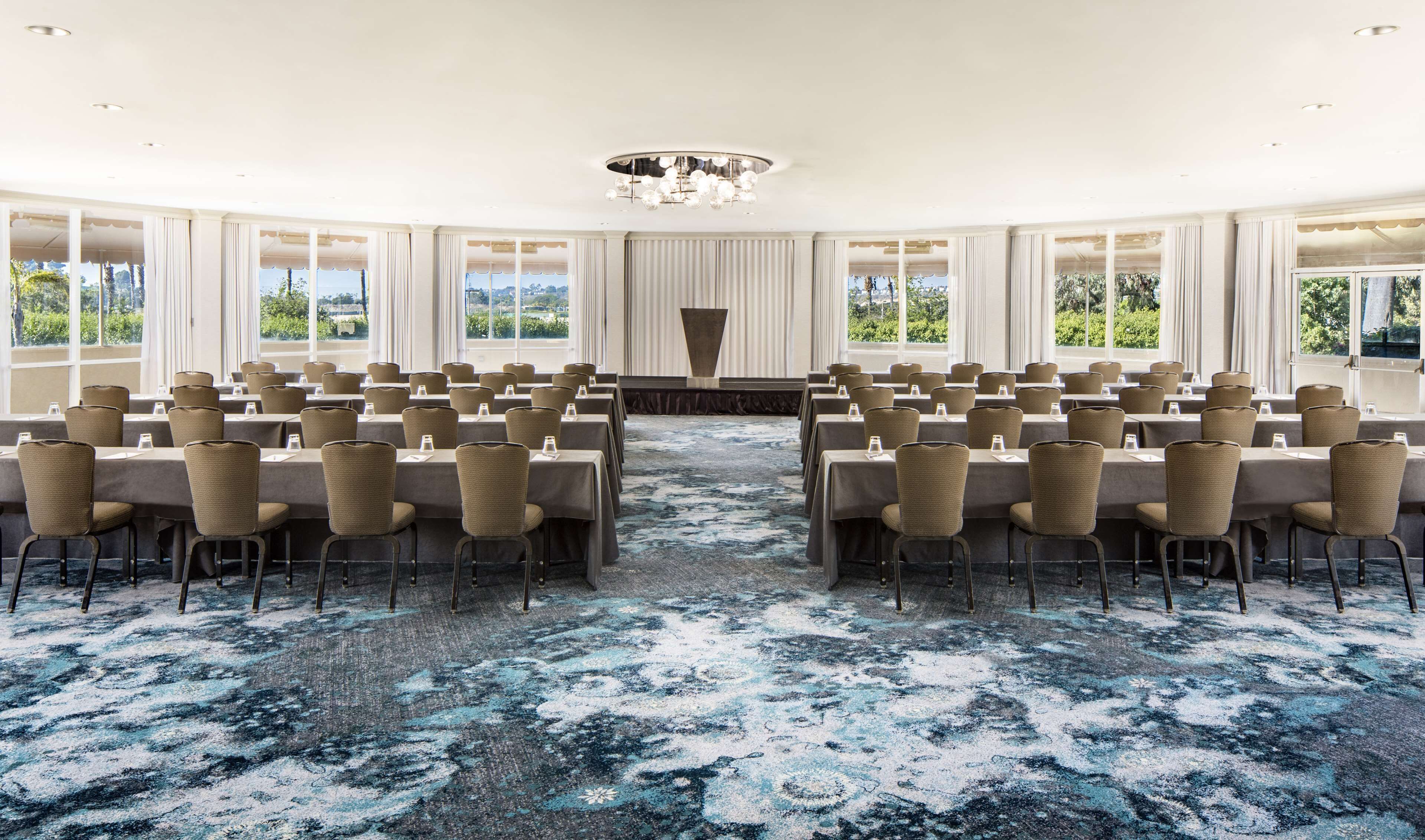 A conference room with rows of tables and chairs, large windows, and a chandelier.