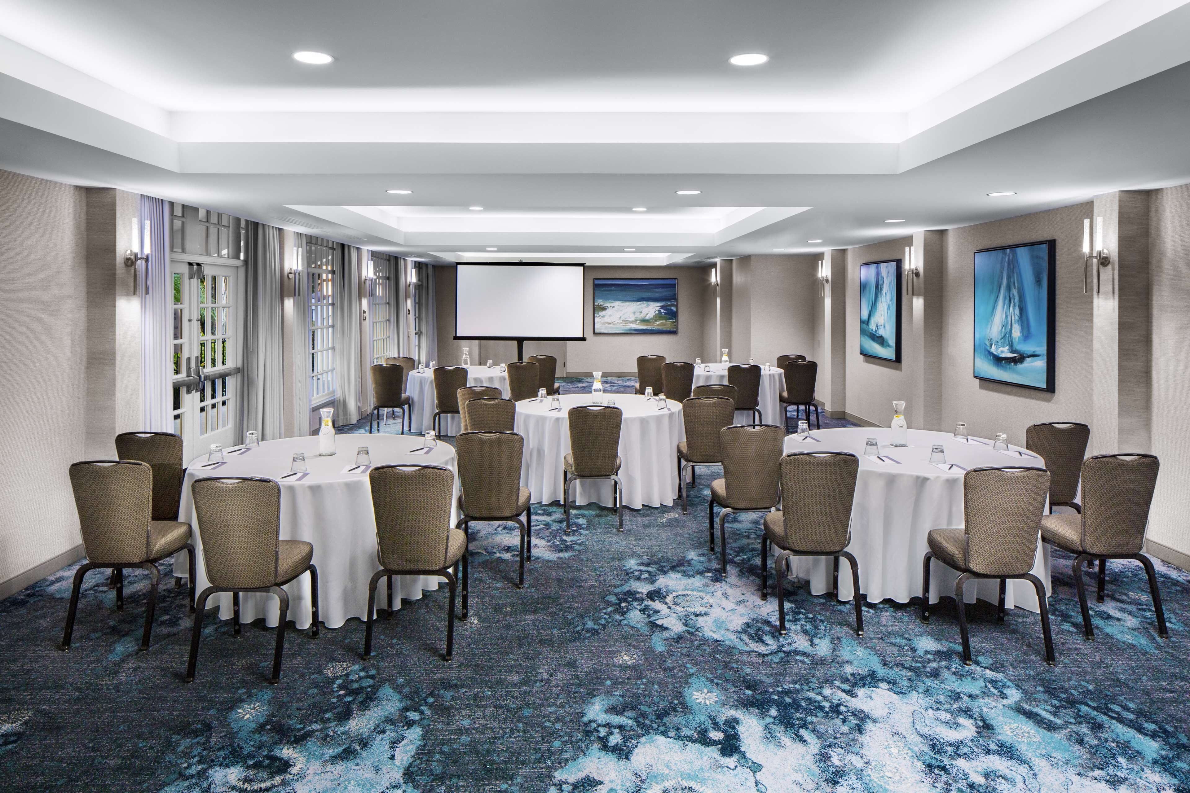 A conference room with round tables, chairs, a projector screen, and artwork on the walls.