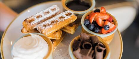 A plate with waffles, a bowl of strawberries, a bowl of chocolate, and a bowl of whipped cream.