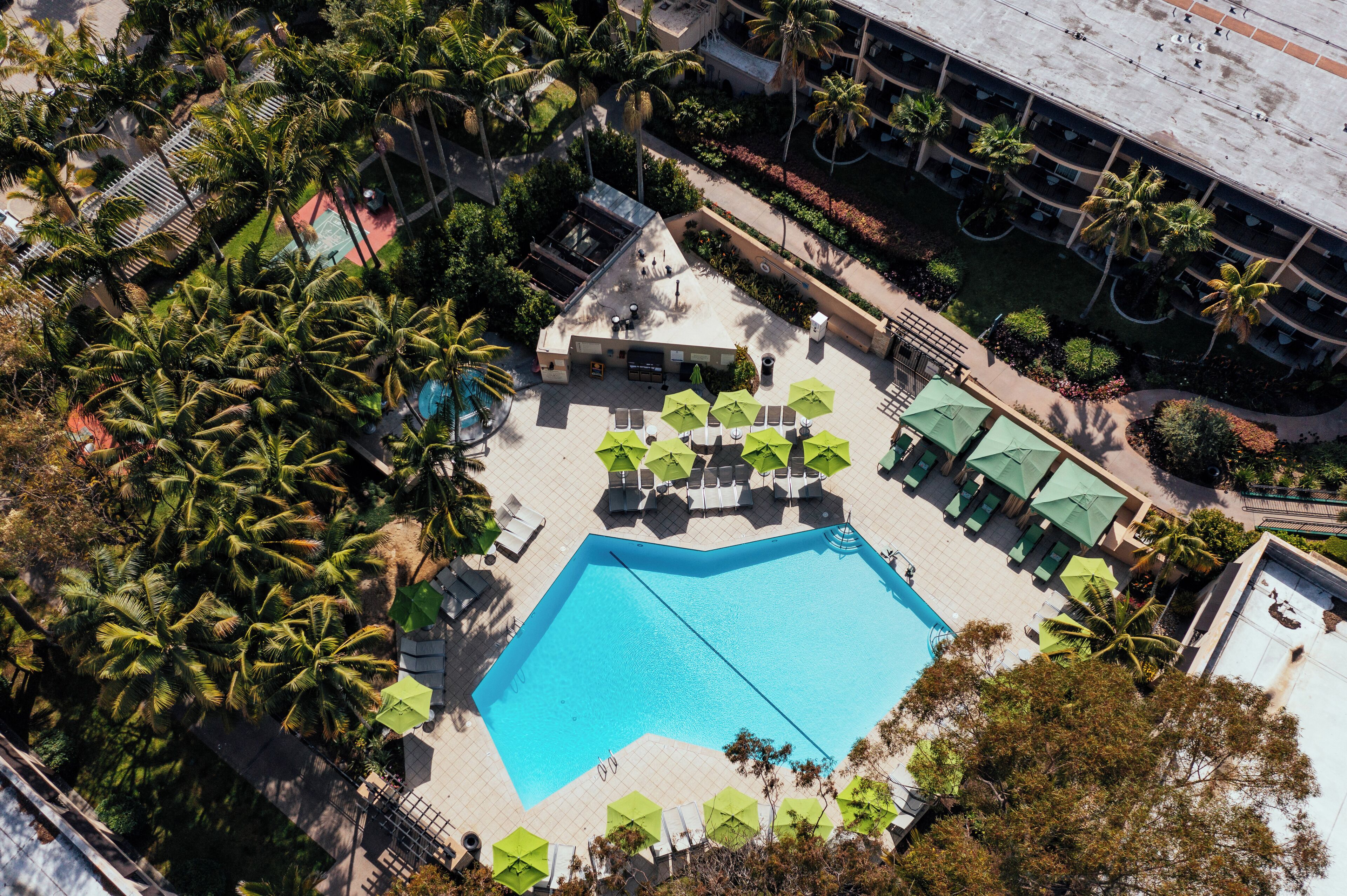 Vista aérea de un hotel con una piscina central, rodeado de palmeras y zonas de estar al aire libre.