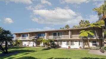 A two-story hotel with a balcony on each floor, surrounded by well-maintained lawns and palm trees.
