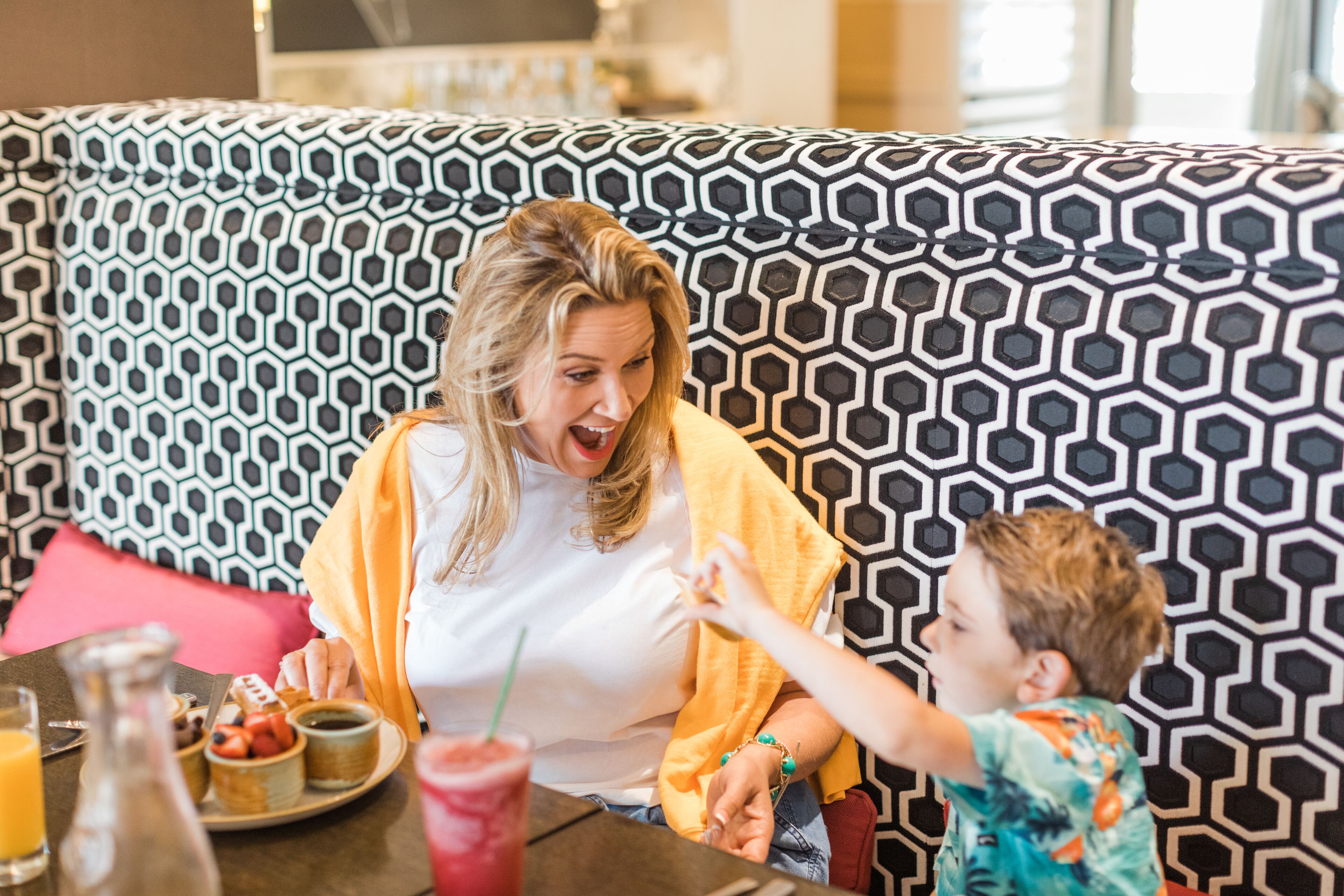 Un coin repas avec un mur décoré de motifs, une table où sont disposés des aliments pour le petit-déjeuner, et une personne et un enfant assis.