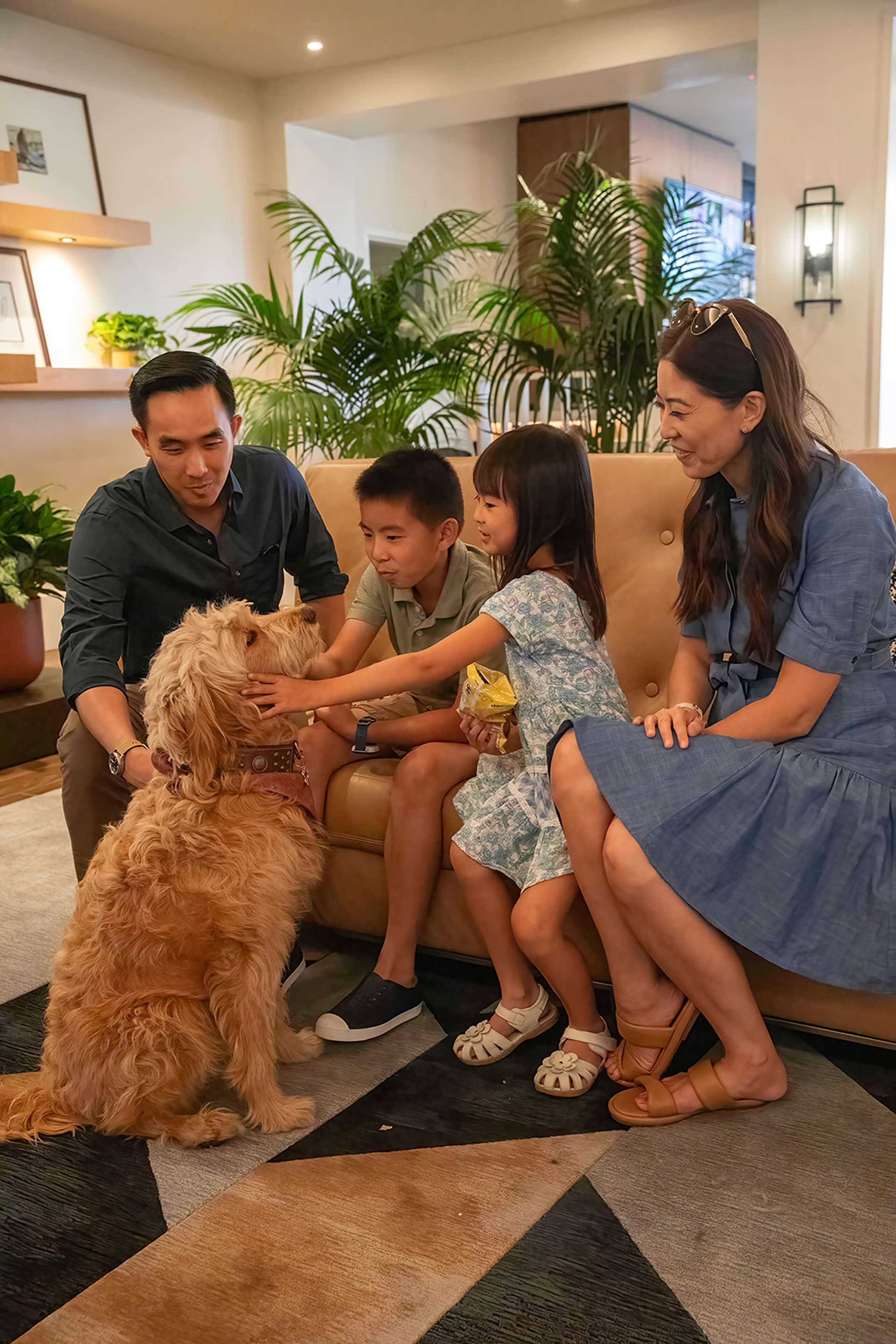 Eine Familie sitzt mit einem Hund auf einer Couch, umgeben von Zimmerpflanzen und einem modernen Interieur.