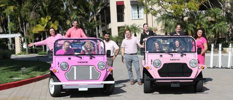 Two pink MOKE vehicles parked on a paved area with people standing beside them.