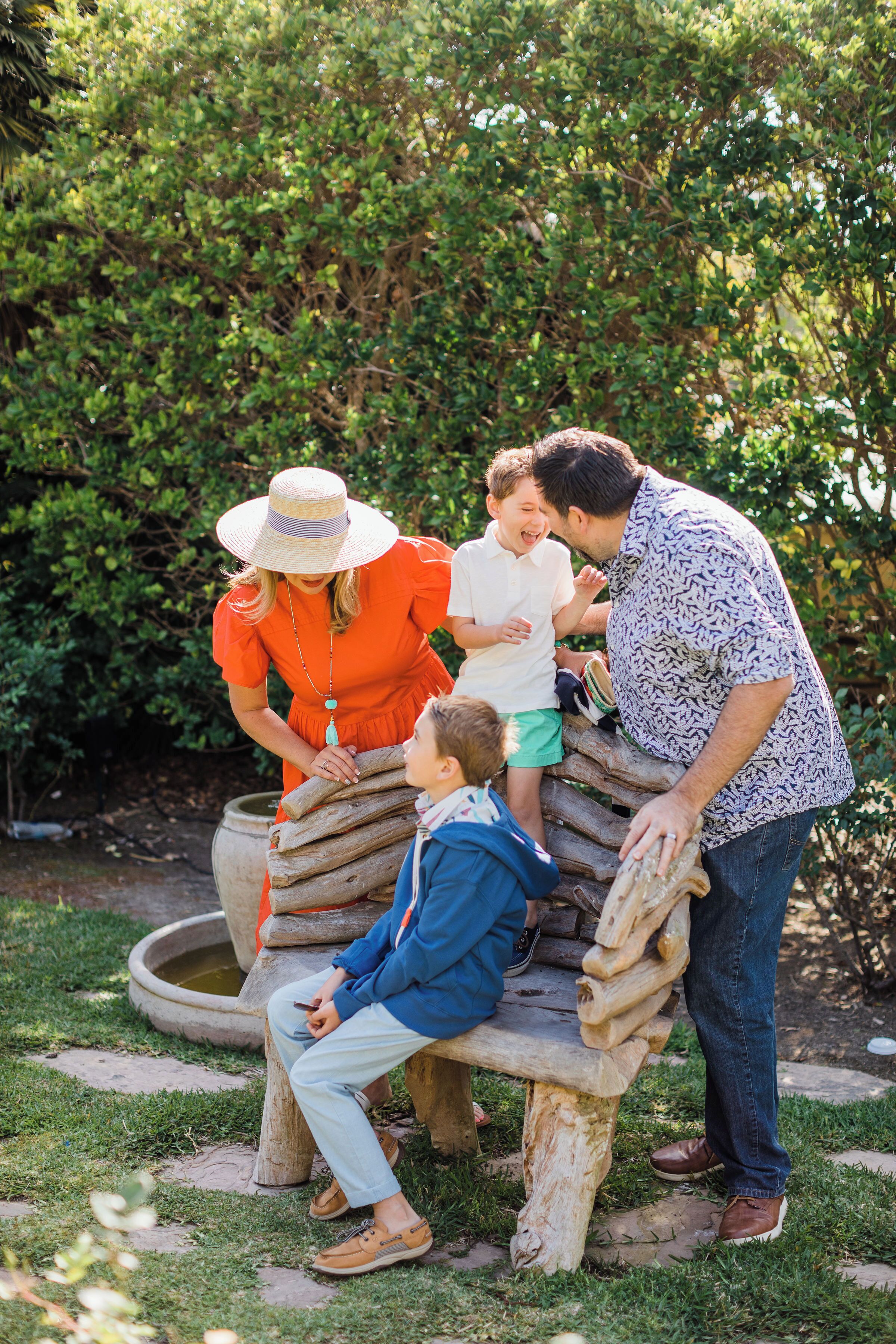 A family sitting on a wooden bench in a garden with greenery in the background.