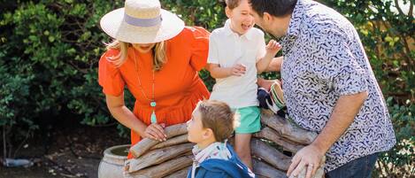 A family sitting on a wooden bench in a garden with greenery in the background.