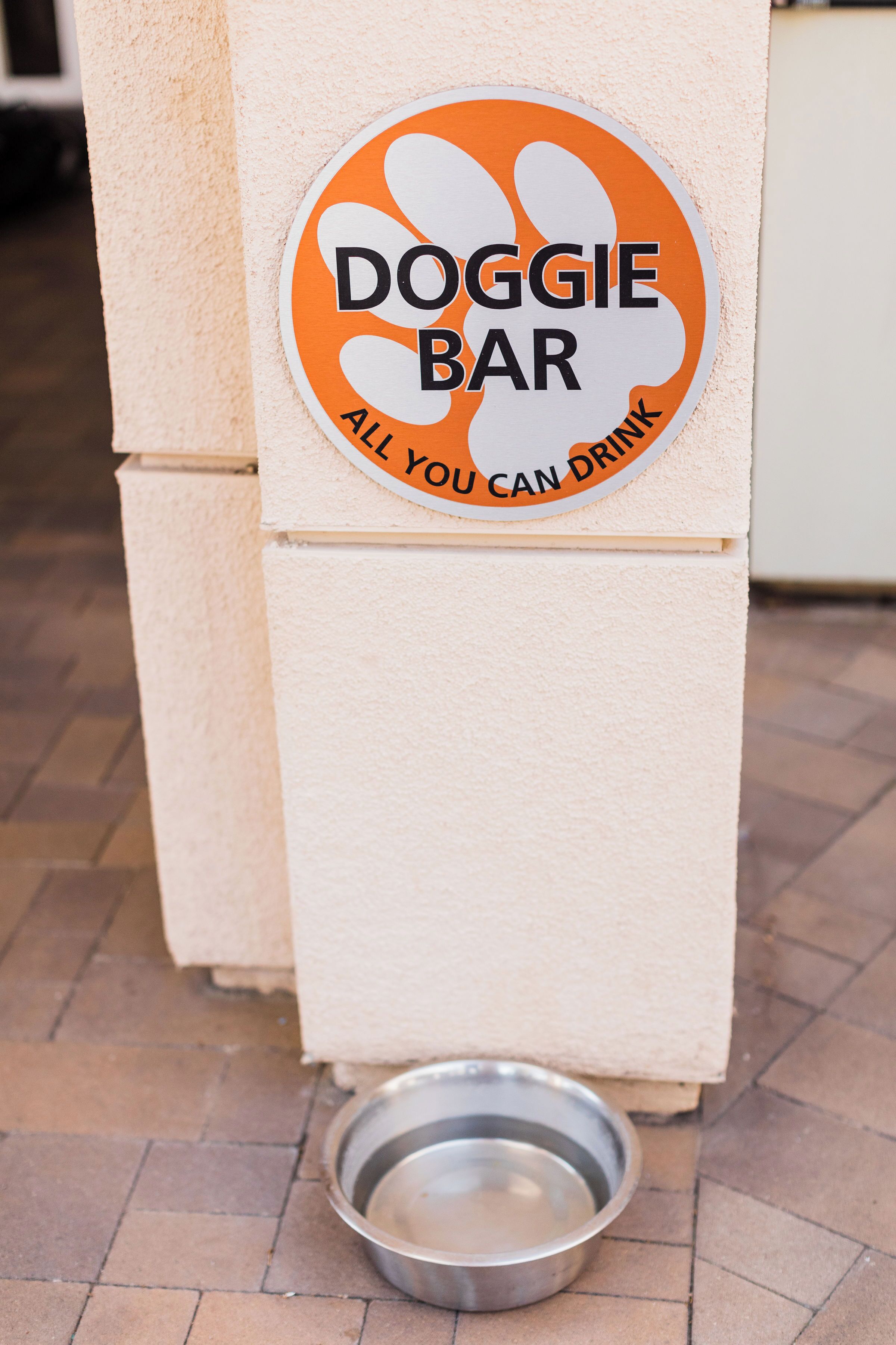 A DOGGIE BAR sign with a metal bowl on the ground.