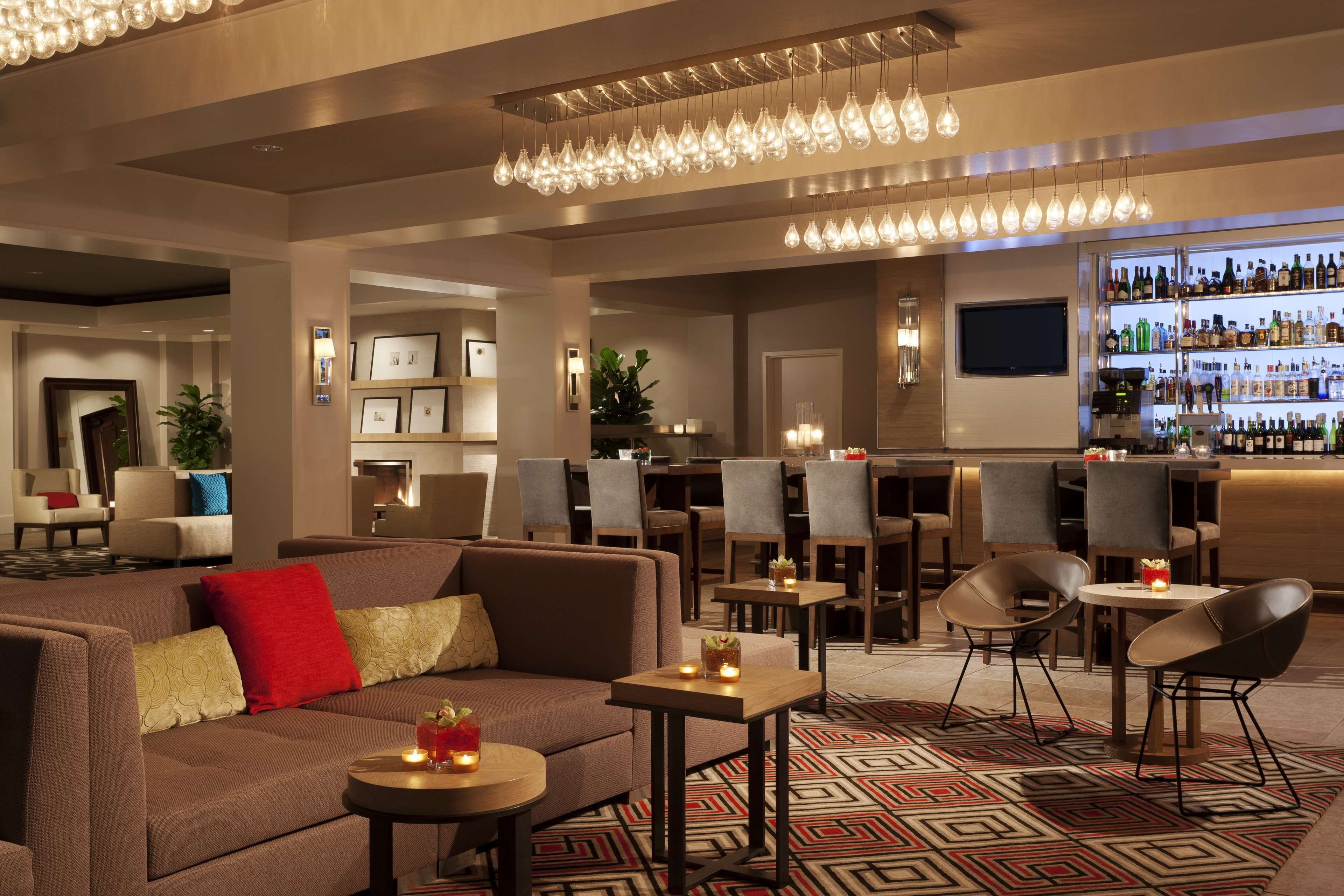 Un moderno hall de hotel con zona de bar, arreglos de asientos y una pantalla de televisión.
