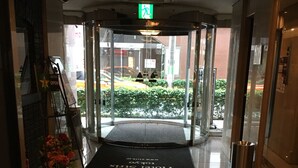 A hotel entrance with a revolving door, a glass door, a sign indicating the hotel name, and a flower arrangement on the left. - Hotel Strix Tokyo (Tokyo)