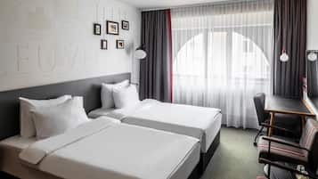 Une chambre d’hôtel avec deux lits, un bureau et une chaise. Les murs sont ornés de tableaux encadrés et il y a une carte.