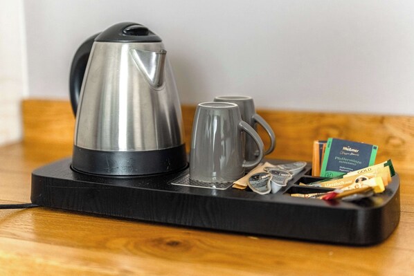 Una tetera de acero inoxidable sobre una bandeja negra, con dos tazas de vidrio y varios objetos encima.