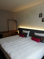 Una habitación de hotel con una cama grande, un cabecero con un mapa y un escritorio con una lámpara.