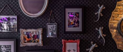A wall with various framed pictures and decorative items, including a mirror and lizards.
