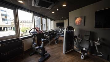 A gym with exercise equipment, large windows, and a view of buildings outside.