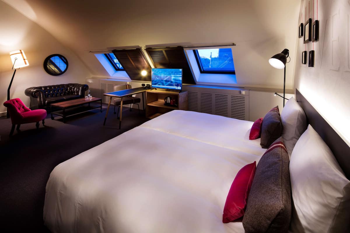 A modern hotel room with a large bed, a desk, a sofa, and skylights.