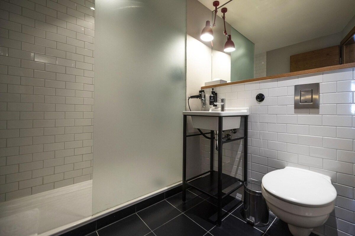 A modern bathroom with white subway tiles, a black tiled floor, a white toilet, a glass shower enclosure, and a wooden countertop above the sink.