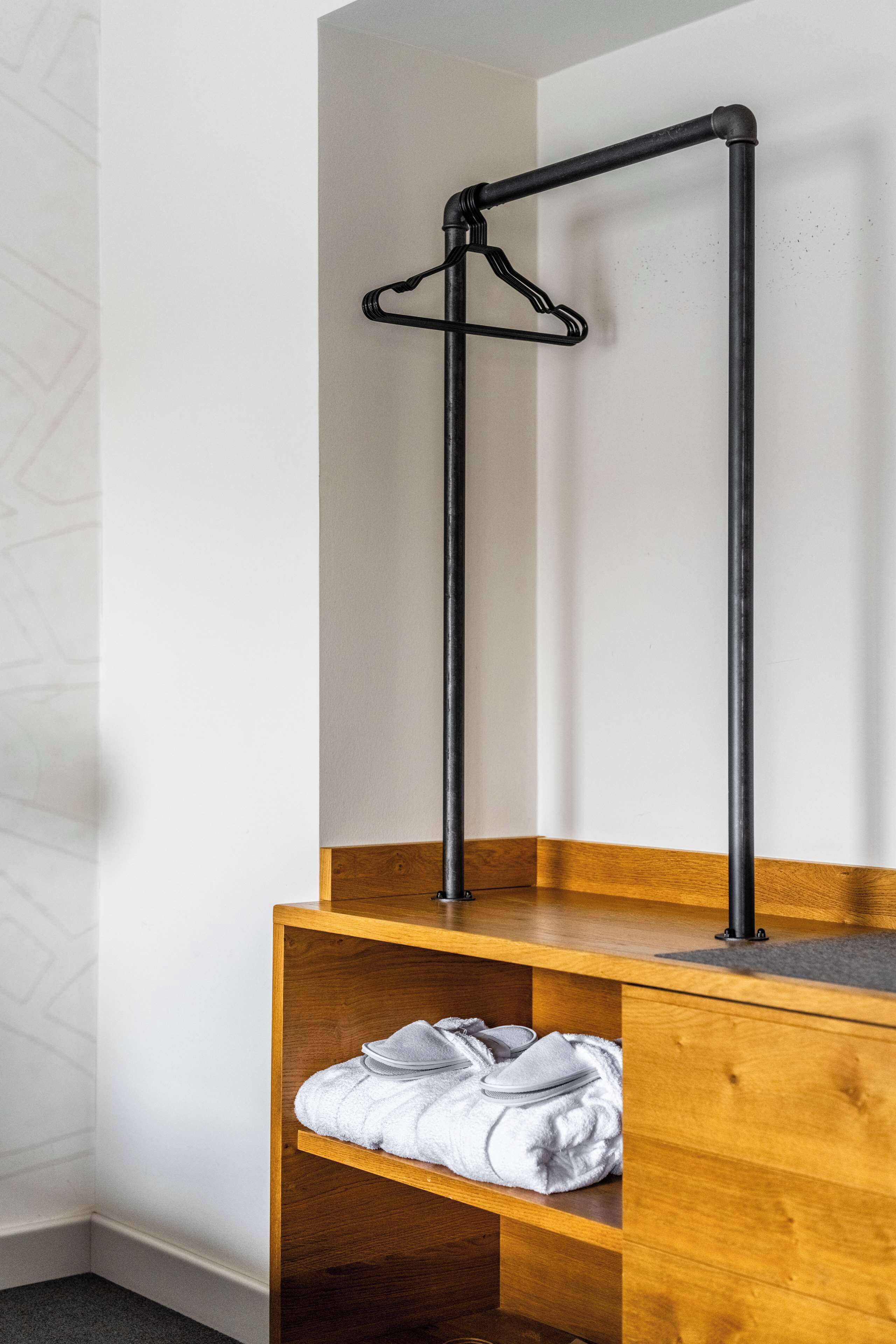 Esquina de una habitación con un banco de madera y un perchero de metal negro.