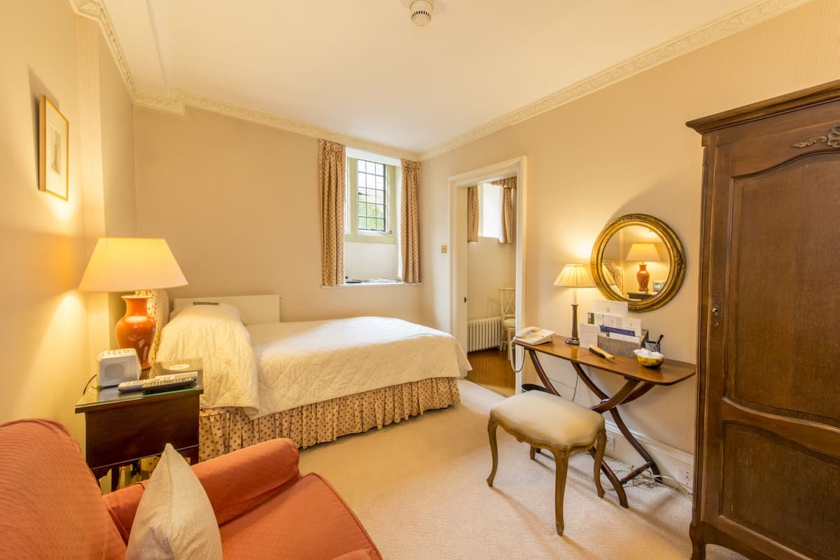 A hotel room with a bed, a desk with a chair, a wardrobe, and a window with curtains.