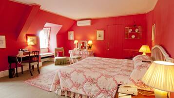 A bedroom with a sloped ceiling, a bed with a floral bedspread, two bedside tables with lamps, a desk with a chair, and a window with curtains.