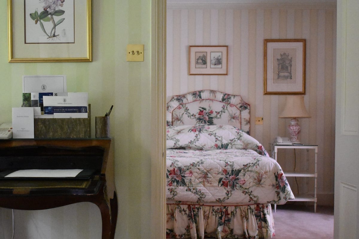 A bedroom with a floral bedspread, a piano, and framed pictures on the wall.