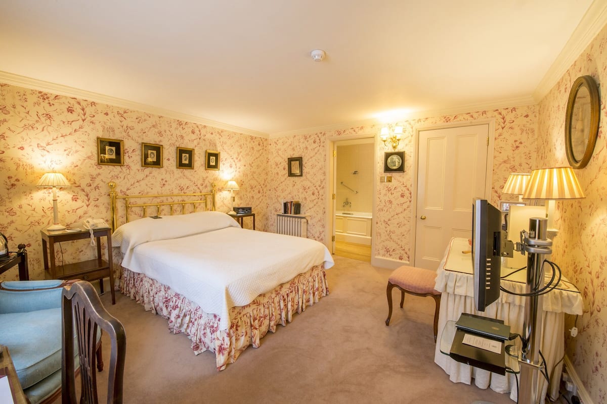 A bedroom with a large bed, a desk with a computer, a chair, and a bathroom door.