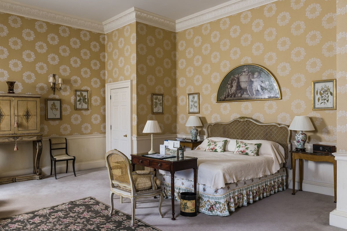 A classic bedroom with a large bed, two bedside tables with lamps, a desk, and a chair.