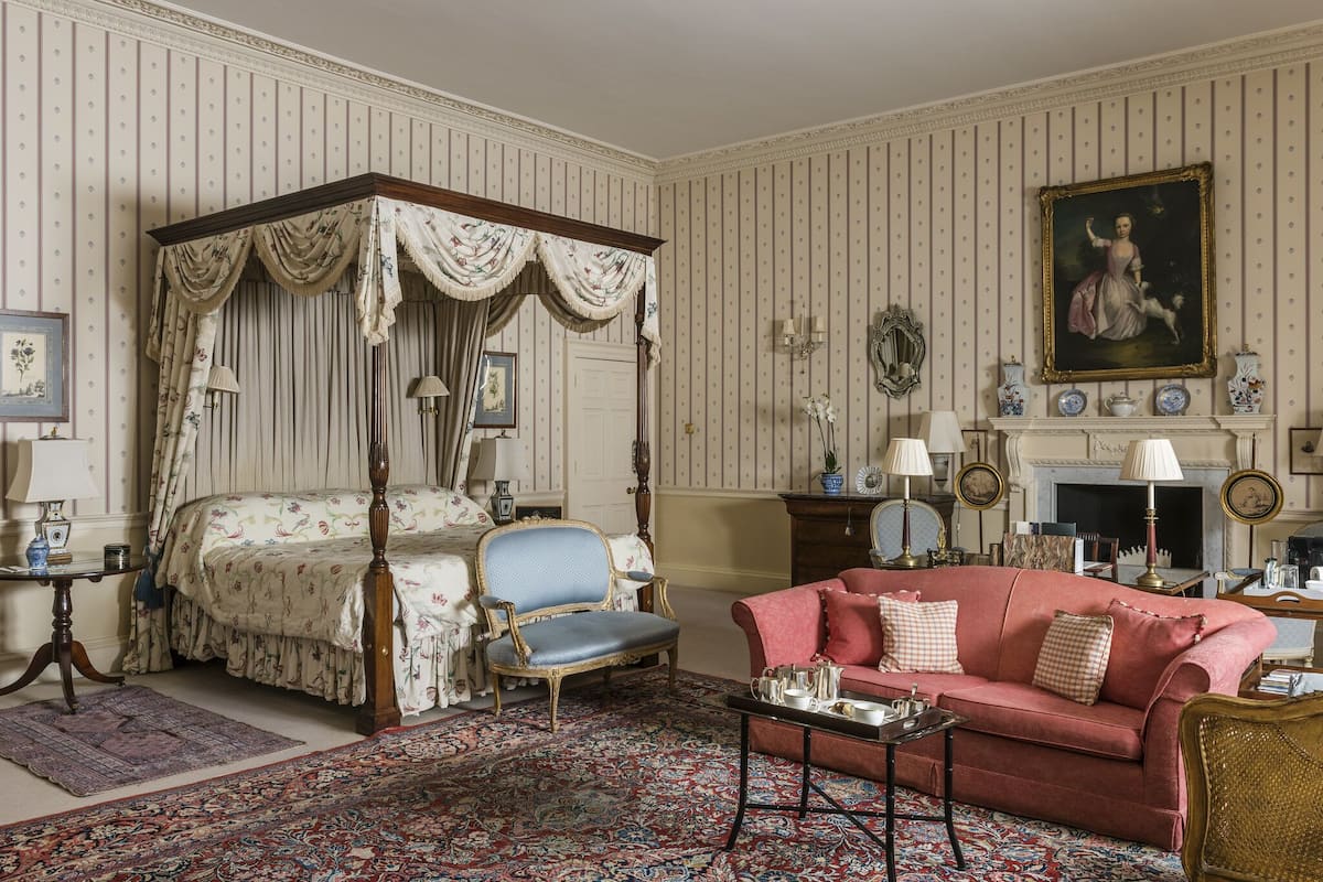 A room with a four-poster bed, a red sofa, a patterned rug, and a painting on the wall.