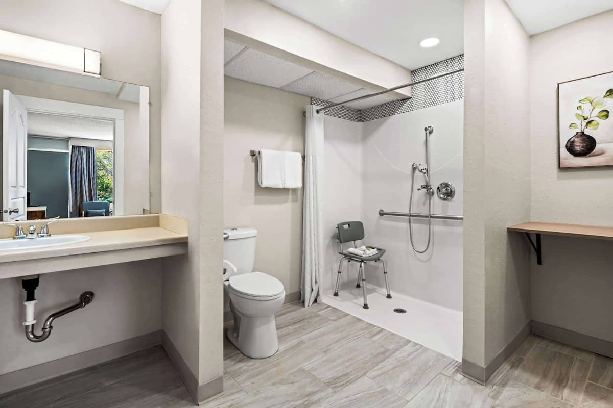 A modern bathroom with a toilet, sink, shower, and a chair.