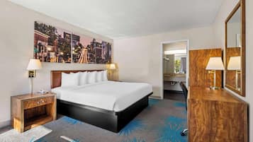 A hotel room with a large bed, a nightstand, a desk with a mirror, and a cityscape painting on the wall.