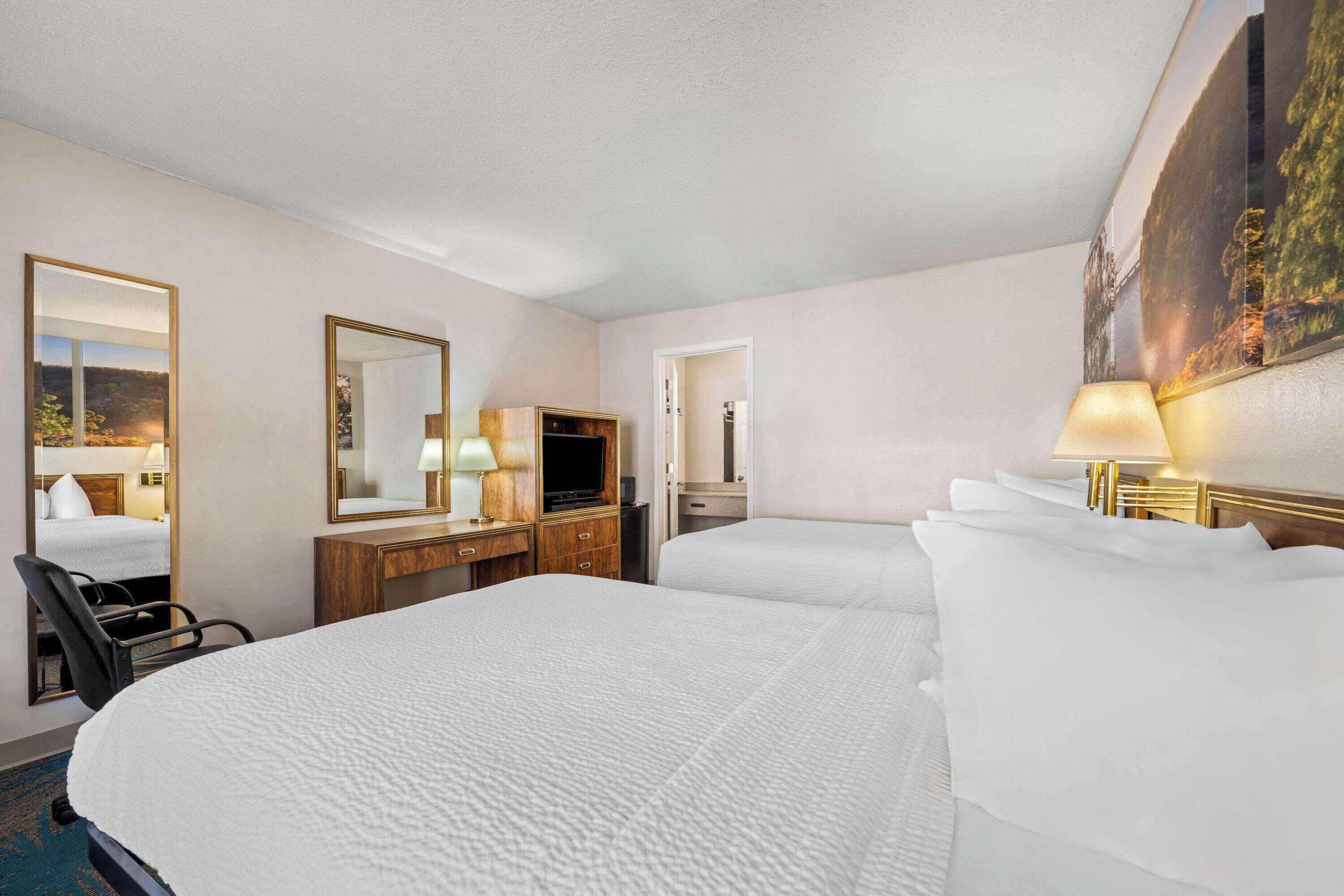 A hotel room with two beds, a desk with a TV, a chair, and a painting on the wall.