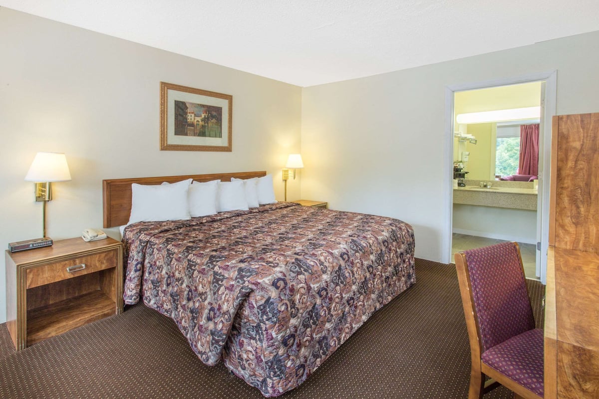 A hotel room with a bed, bedside lamps, a chair, a wooden nightstand, and a framed picture on the wall.