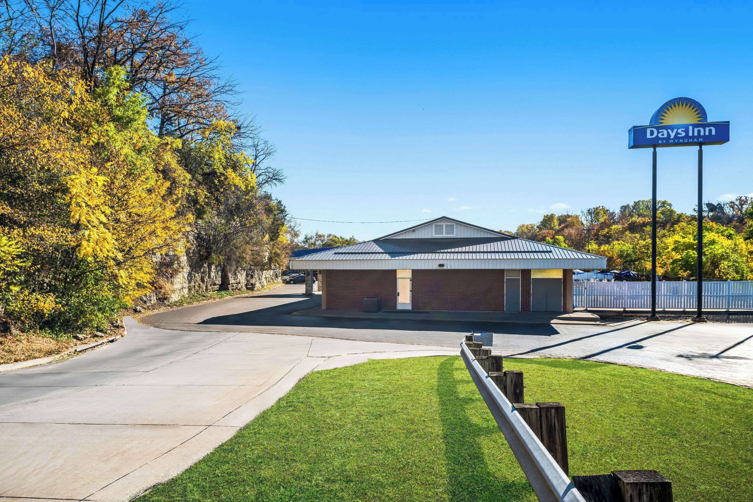 A Days Inn with a brick building and a metal roof, surrounded by trees and a well-maintained lawn.