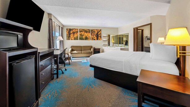 A hotel room with a bed, a desk, a television, a sofa, and a bathroom visible through an open door.